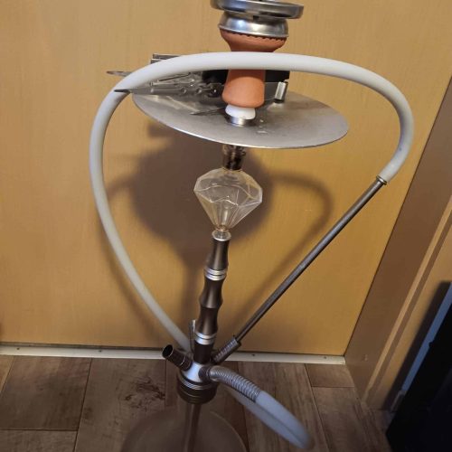 Shisha mit Rauchsäule und Zubehör, auf Holzboden stehend.