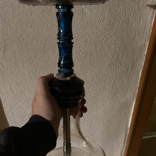 Rauchsäule für Shisha mit Glasbasis und Metalldeckel, handgehalten, gegen Wand gehalten.