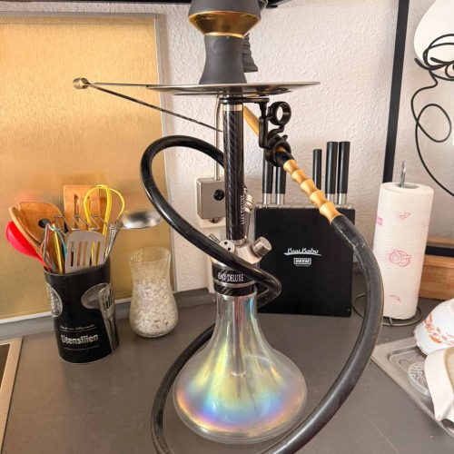 Shisha mit Glasbowl, Schlauch und Zubehör auf Tisch.