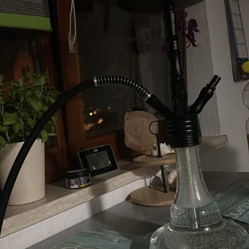 Shisha auf Tisch mit Rauchsäule und Zubehör im Raum.