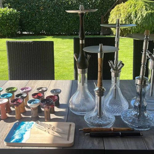 Verschiedene Glasbowl und Shisha-Zubehör auf Tisch im Garten.