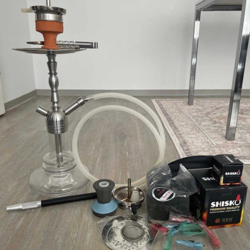 Shisha mit Glasbowl, Schlauch und Zubehör auf Boden.