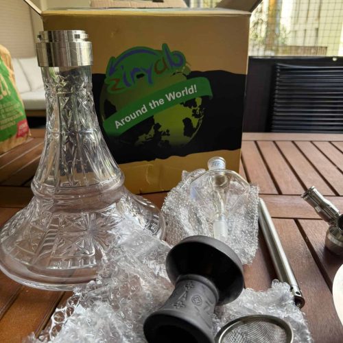 Shisha-Set mit Glas, Silikonschlauch und Zubehör auf Tisch.