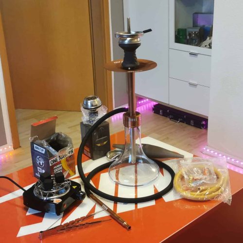 Shisha mit Glasbowl, Schlauch und Tabak auf Tisch.