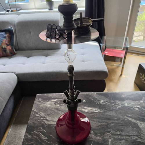 Shisha mit Glasbowl, Schlauch und Zubehör auf Tisch im Wohnzimmer.