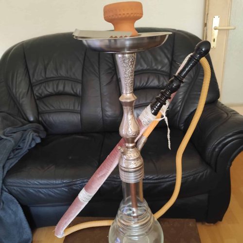 Shisha mit Glasbowl, Schlauch und Metallkopf auf Tisch.