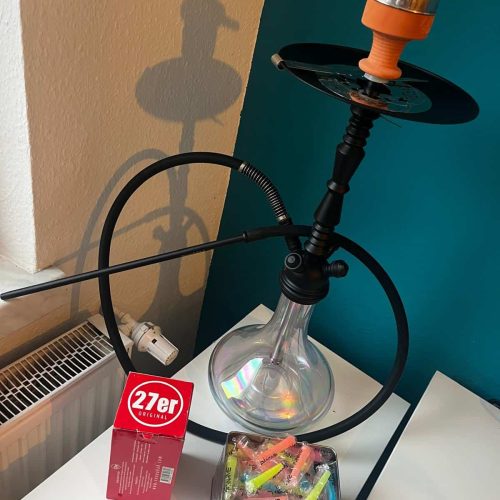 Shisha mit Glasbowl, Schlauch und Zubehör auf Tisch.