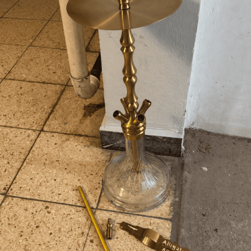 Goldene Shisha mit Glasbowl und Zubehör auf Boden.