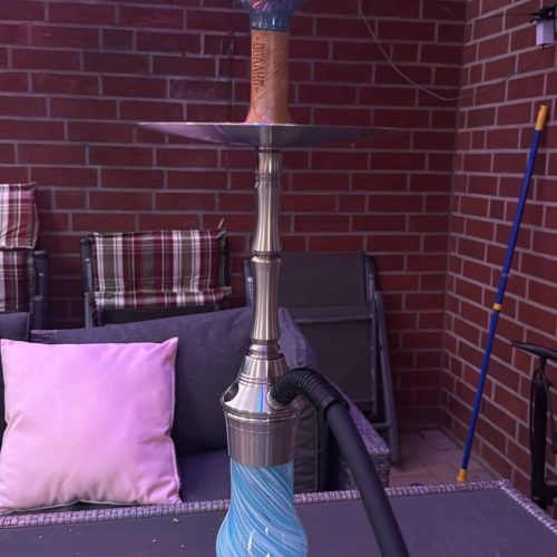 Shisha-Kopf mit bunter Glasbowl auf Terrasse, Backsteinwand im Hintergrund.