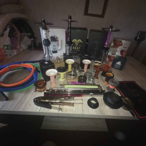 Verschiedene Shisha-Zubehörteile auf einem Tisch, inklusive Glasbowl, Schläuche und Dichtungen.