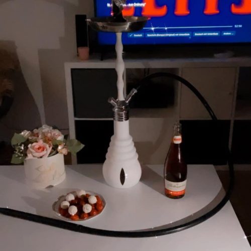 Shisha mit Wasserpfeife, Getränk und Snacks auf Tisch, gemütliche Atmosphäre.
