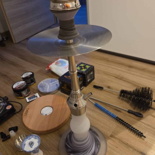 Shisha mit Glasbowl, Kamin, und Reinigungszubehör auf Boden.