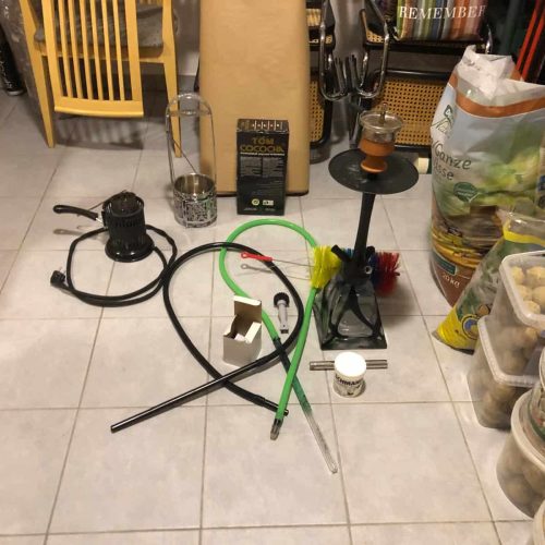 Shisha mit Rauchsäule und Zubehör auf Fliesenboden.