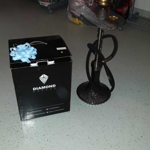 Shisha mit Gold- und schwarzen Elementen, Zubehör und Verpackung im Hintergrund.