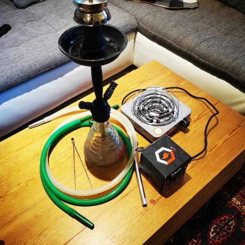 Shisha mit Rauchsäule, Schlauch und Heizgerät auf Tisch.