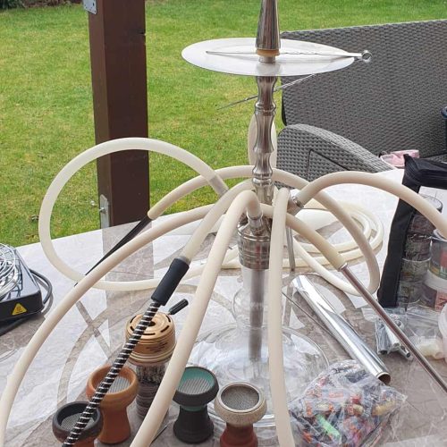Shisha mit mehreren Schläuchen auf einem Tisch im Garten, bereit zum Rauchen.