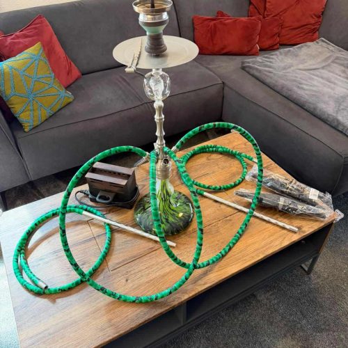 Shisha mit Glasbowl, Schlauch und Zubehör auf Couchtisch.