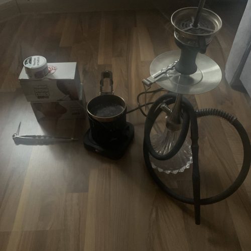 Shisha mit Rauchsäule, Tabak und Zubehör auf Holzboden.