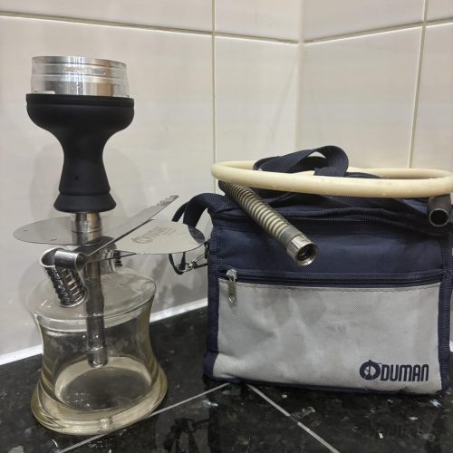 Shisha-Glasbowl mit Schlauch und Tasche auf Fliesenboden.