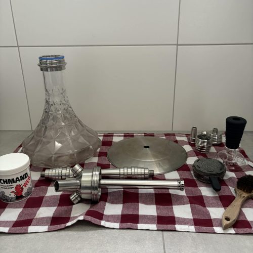 Glas-Shisha mit verschiedenen Teilen und Zubehör auf Tisch.
