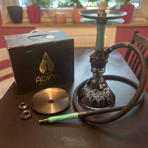 Shisha mit Glasbowl, Schlauch und Zubehör auf Tisch.