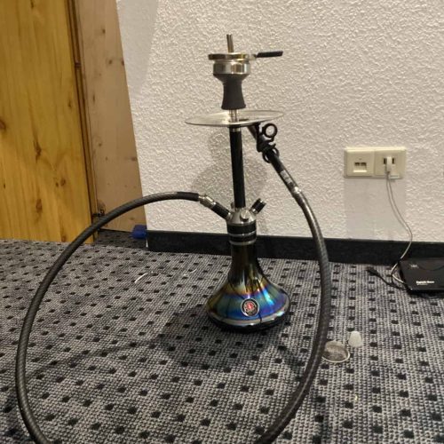 Shisha mit Glasbowl, Schlauch und Metallaufsatz auf Teppichboden.