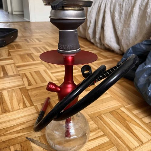 Rauchsäule mit Shisha, Schlauch und Zange auf Holzboden, Wohnzimmer-Setup.