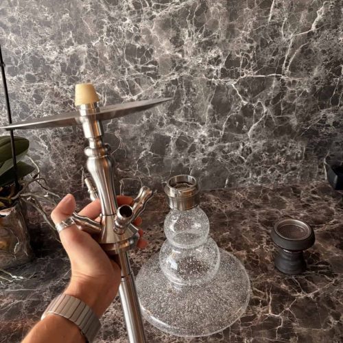 Hand hält Shisha mit Metallrohr und Glasbowl auf Marmoroberfläche.