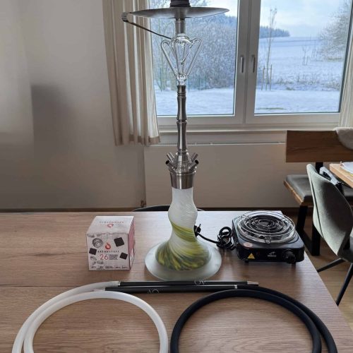 Shisha mit Glasbowl, Schlauch und Heizplatte auf Tisch.