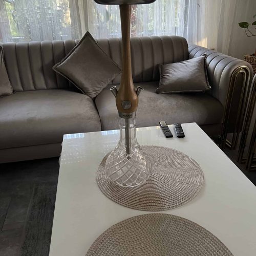 Moderne Hanf-Shisha auf weißem Tisch mit Couch im Hintergrund.