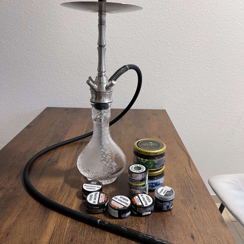 Schöne Shisha mit Glasgefäß und Tabakdosen auf Holztisch.