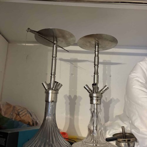 Zwei Glas-Shishas mit Metallaufsätzen auf einem Tisch.
