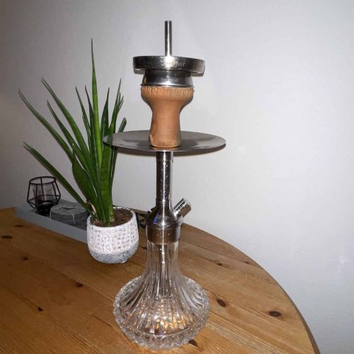 Rauch-Hookah mit Glasbasis und Metallaufsatz, auf Holztisch.