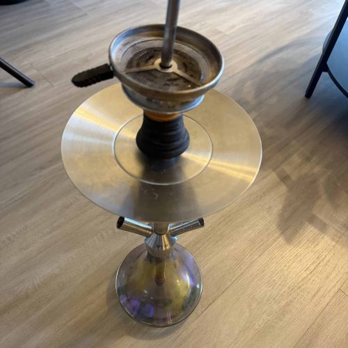 Alte Shisha mit Glasbowl und Metallstange auf Tisch.