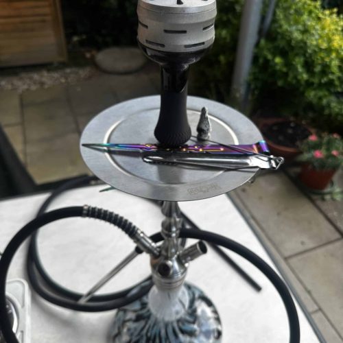 Rauchsäule mit Shisha, Kopf und Zange auf einem Tisch im Garten.