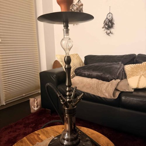 Dekorative Shisha auf einem Tisch im Wohnzimmer, mit Sitzgelegenheiten im Hintergrund.
