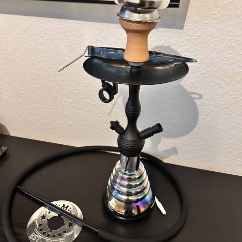 Shisha mit Glasbowl, Schlauch und Zubehör auf Tisch.