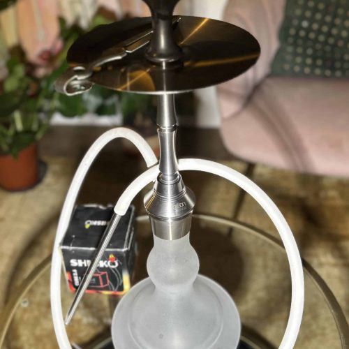 Shisha mit Glasbowl, Silikonschlauch und Metallkopf, auf Tisch.