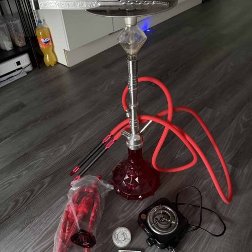 Shisha mit Glaskolben, Schlauch und Zubehör auf Holzboden.