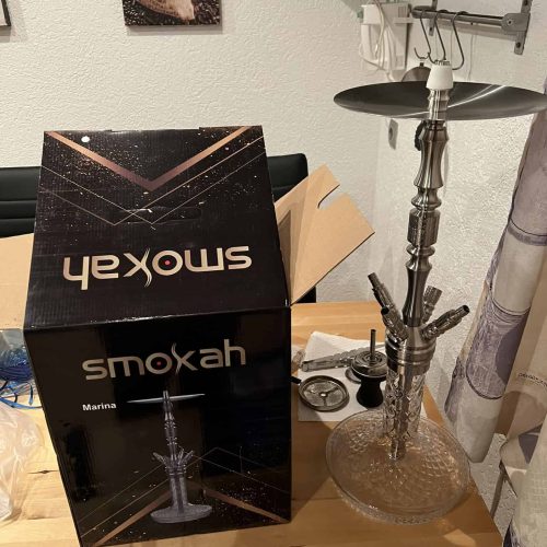 Shisha mit Glasbowl, Schlauch und Zubehör auf Tisch.