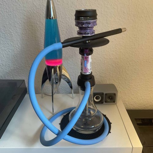 Moderne Shisha mit blauer Rauchsäule und Zubehör auf Tisch.