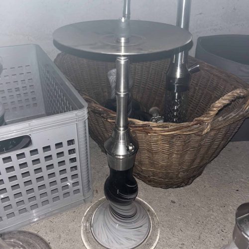 Shisha mit Glasbowl, Metallaufsatz und Zubehör im Hintergrund.
