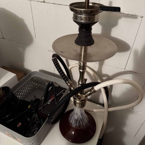 Shisha mit Rauchsäule, Kopf und Schlauch, auf Tisch.
