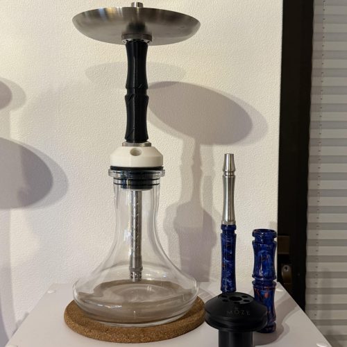 Shisha mit Glasbowl, Tabakkopf und Zubehör, auf weißem Tisch.