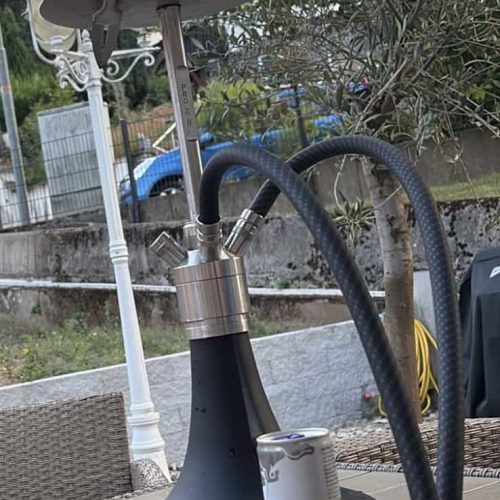 Shisha mit schwarzer Glasbowl, Schlauch und Kohleteller im Garten.