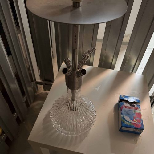 Shisha-Kopf mit Glasbasis und Metallaufsatz auf Tisch.