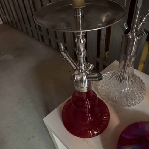 Shisha mit Glas- und Metallteilen, auf weißem Tisch in Raum.
