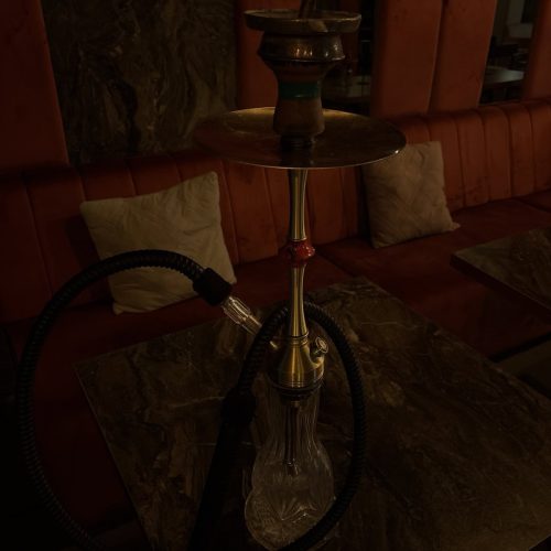 Shisha mit Glasbowl auf Tisch in Lounge-Umgebung.