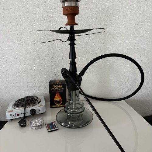 Shisha mit Rauchsäule, Kohle und Zubehör auf Tisch.