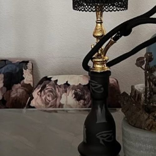 Wasserpfeife mit schwarzem Kopf und goldenen Akzenten auf einem Tisch.
